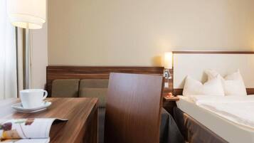 Ein Hotelzimmer mit Bett, Schreibtisch mit Tasse und Untertasse, Sessel und Nachttisch mit Lampe.