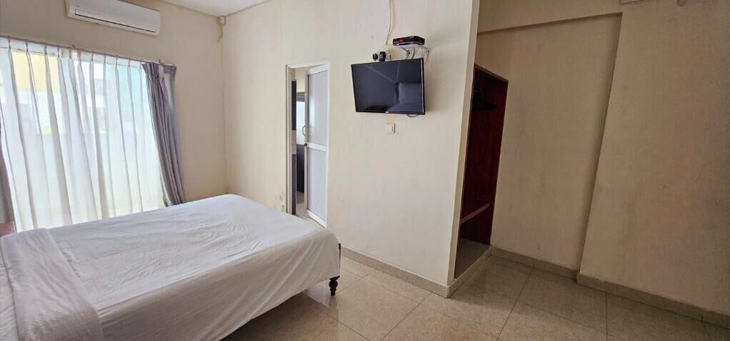 Una habitación con una cama, un televisor en la pared y un ventanal con cortinas.