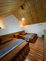 A room with two beds, wooden flooring, a sloped ceiling, and a hanging light fixture.
