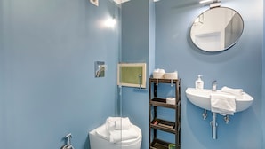 A bathroom with a white toilet, a round mirror, a white sink, and a shelf with toiletries. - Casetta Azzurra Flat With Parking in Capalbio (Capalbio)