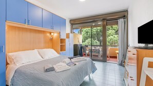 A hotel room with a bed, a TV, a desk, and a balcony with a table and chairs. - Casetta Azzurra Flat With Parking in Capalbio (Capalbio)
