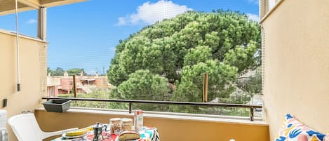 A balcony with a table set for dining, a chair, and a view of a tree.