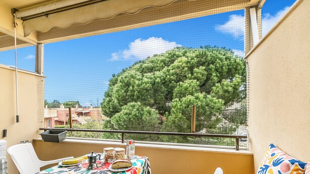 A balcony with a table set for dining, a chair, and a view of a tree. - Casetta Azzurra Flat With Parking in Capalbio (Capalbio)