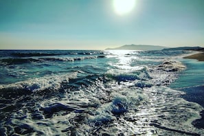 Una playa con olas, cielo despejado y montañas a lo lejos.
