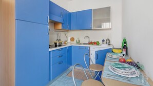 A compact kitchen with blue cabinets, a sink, a dishwasher, and a dining area with a table set for two. - Casetta Azzurra Flat With Parking in Capalbio (Capalbio)