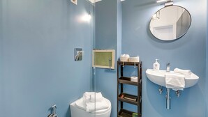 A bathroom with a white toilet, a round mirror, a white sink, and a shelf with toiletries. - Casetta Azzurra Flat With Parking in Capalbio (Capalbio)
