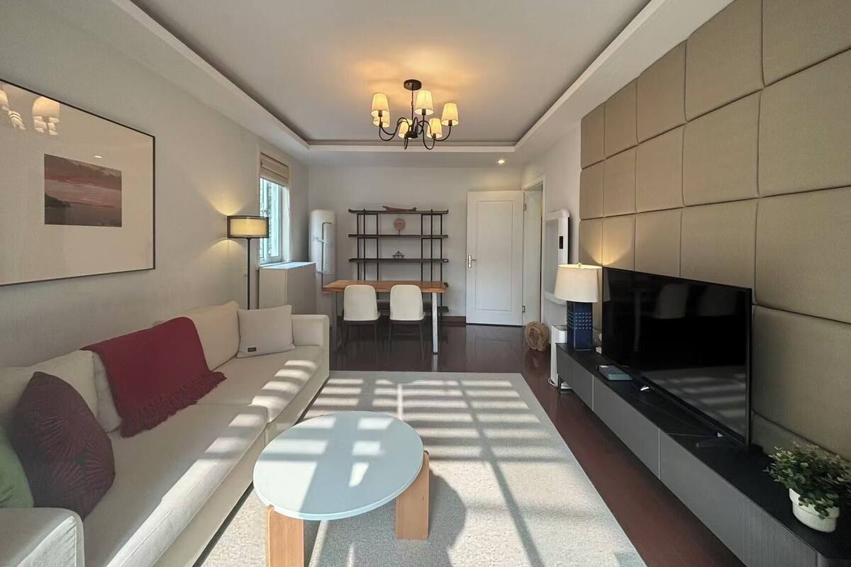 A modern living room with a sofa, a round coffee table, a TV, and a chandelier.
