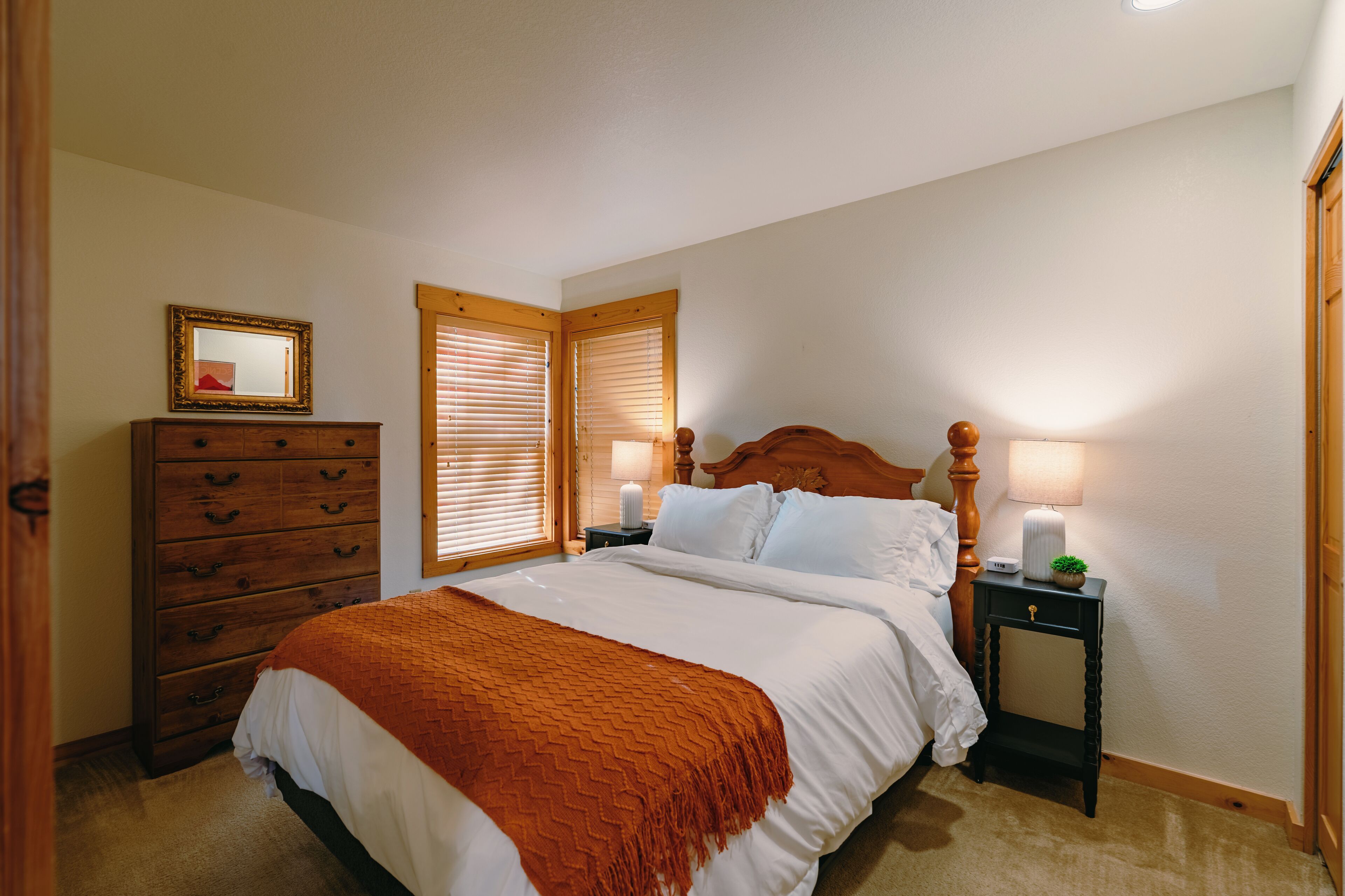 Een slaapkamer met een bed, een houten dressoir, twee nachtkastjes met lampen en een spiegel aan de muur.