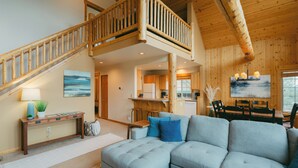 A spacious living area with a large gray sectional sofa, a wooden staircase, and a kitchen in the background.