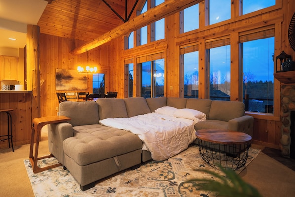 A cozy log cabin interior with a large sofa, a dining area, and a fireplace.