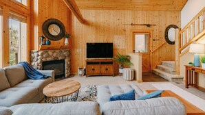 A wooden interior with a stone fireplace, a television, sofas, and a staircase.