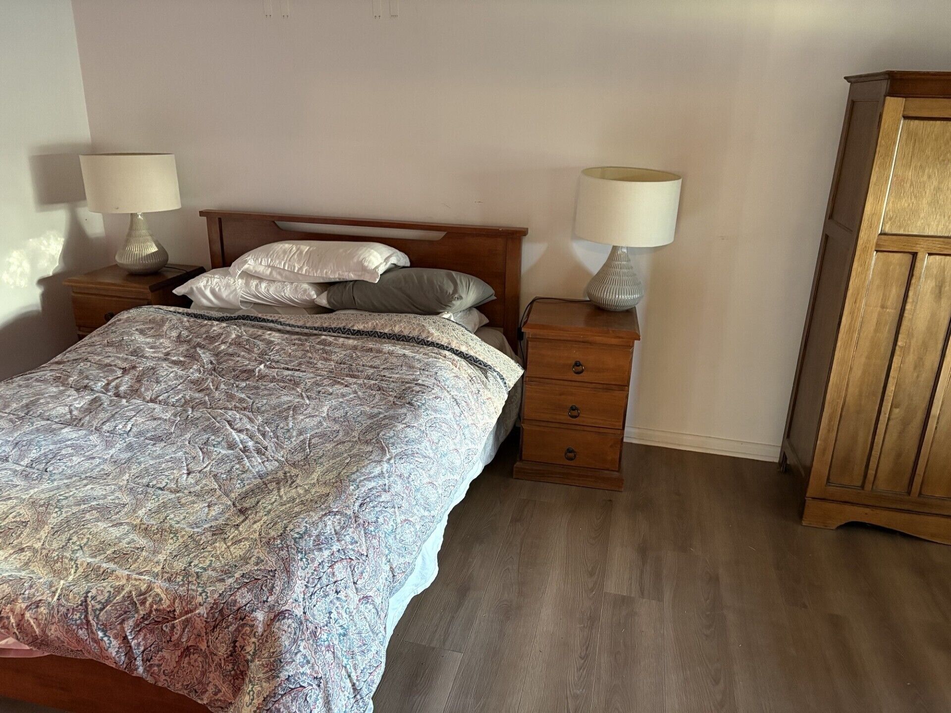 A bedroom with a bed, two nightstands, a wooden wardrobe, and a patterned bedspread.