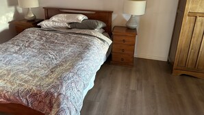 Un dormitorio con cama, dos mesitas de noche, un armario de madera y una colcha estampada.
