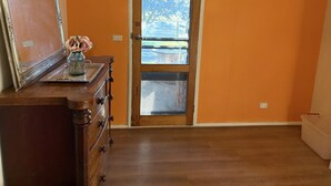 Una habitación con un aparador de madera, una puerta que da al exterior y un florero con flores sobre el aparador.