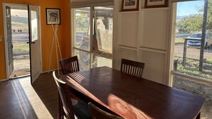 Un comedor con una mesa y sillas de madera, una ventana con vista a un estacionamiento y cuadros en la pared.