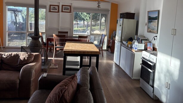 Un amplio salón con mesa de comedor, sofás, una cocina con estufa y ventanas grandes.