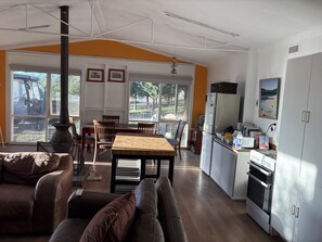Un amplio salón con mesa de comedor, sofás, una cocina con estufa y ventanas grandes.