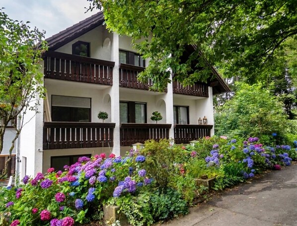 A multi-story building with balconies, surrounded by lush greenery and vibrant flowers. - Belvilla Heiderhof 1-bedroom Apartment (Obersteinebach)