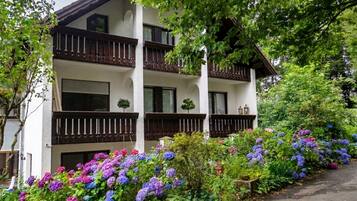A two-story building with balconies, surrounded by lush greenery and vibrant flowers.
