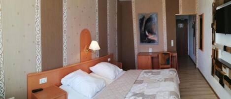 Una camera d'albergo con un letto, comodino, lampada, scrivania, sedia e un quadro appeso al muro.