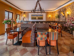 A restaurant with a long communal table, booths with colorful upholstery, and a stone wall with a mounted animal head. - Belvilla Heiderhof 1-bedroom Apartment (Obersteinebach)