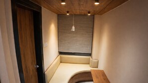 A compact room with a curved bench, a small table, a window with blinds, and a door. - Hotel Regal Crest (Bhubaneshwar)