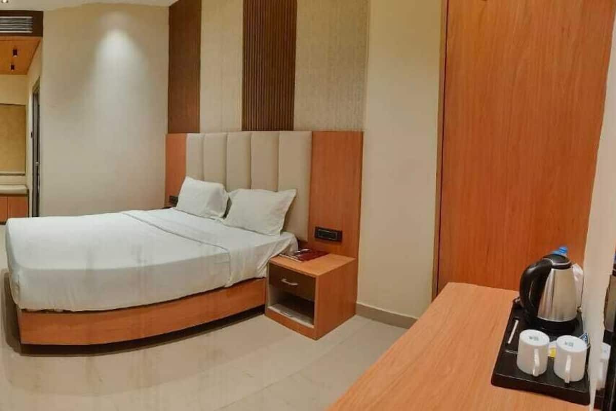 A hotel room with a curved bed, a bedside table, a small seating area, and a coffee machine.
