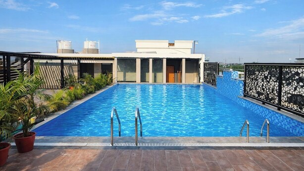 A rooftop swimming pool with a clear view of the sky, surrounded by potted plants and a modern building structure. - Hotel Regal Crest (Bhubaneshwar)