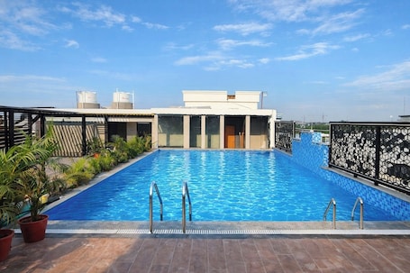 A rooftop swimming pool with a clear view of the sky, surrounded by potted plants and a modern building structure.. Hotel Regal Crest