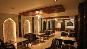 A restaurant with high-backed chairs, tables, and arched windows. - Hotel Regal Crest (Bhubaneshwar)