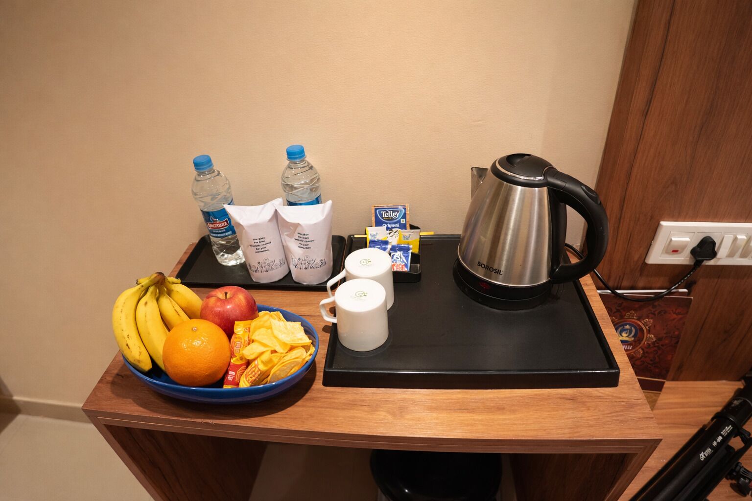 Een ontbijt opstelling met een fruitschaal, een koffiezetapparaat en een waterkoker op een houten tafel.