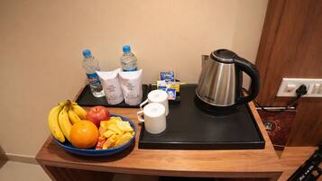 Een ontbijt opstelling met een fruitschaal, een koffiezetapparaat en een waterkoker op een houten tafel.