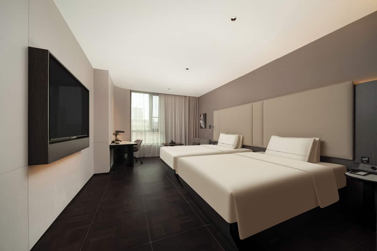 A modern hotel room with two beds, a flat-screen TV, a desk, and a large window.