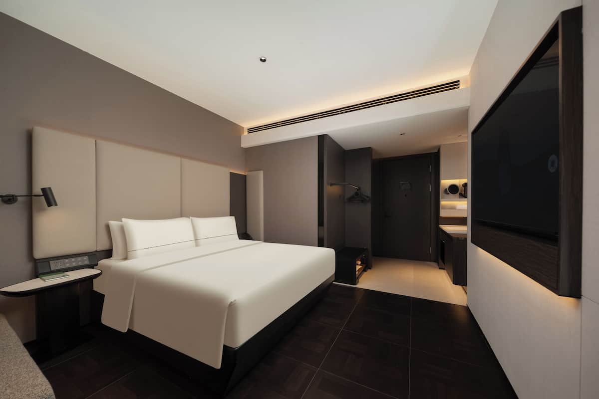 A modern hotel room with a large bed, a bedside table, a built-in TV, and a separate bathroom area.