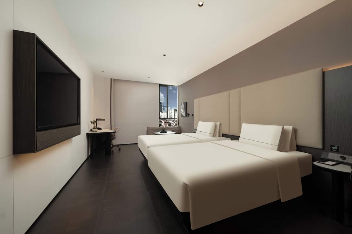 A modern hotel room with a large bed, a desk, a chair, and a TV mounted on the wall.
