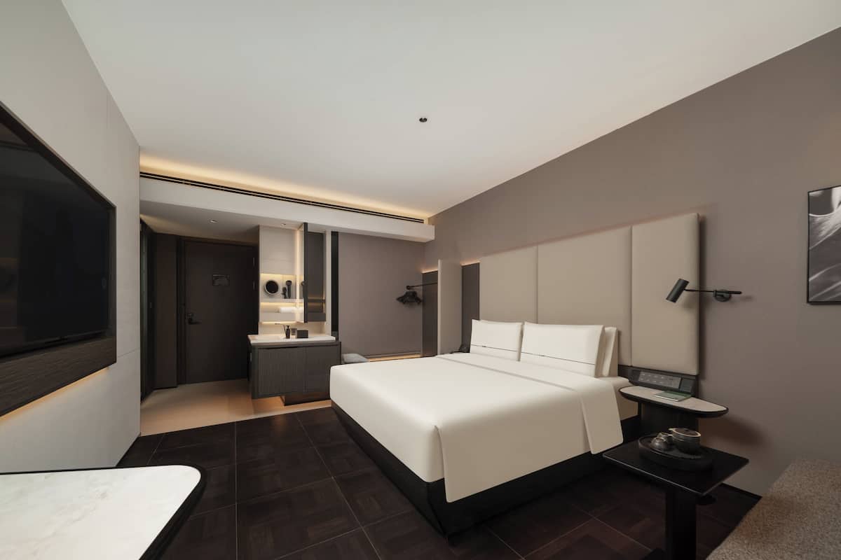A modern hotel room with a large bed, a desk, a TV, and a bathroom.