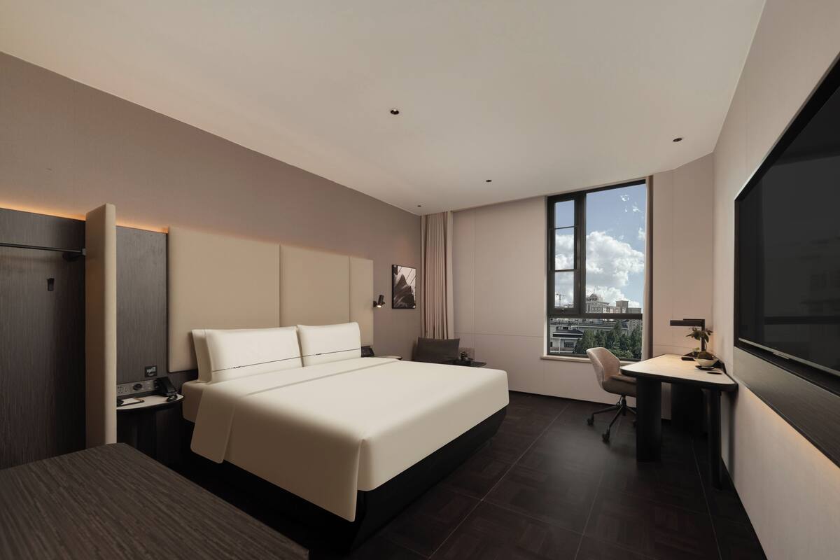A modern hotel room with a large bed, a desk, and a city view.