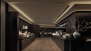 A modern, dimly lit bar area with a long counter, recessed lighting, and a decorative vase.