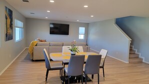 Una sala de estar moderna con comedor, un sofá, un televisor de pantalla plana y una escalera.