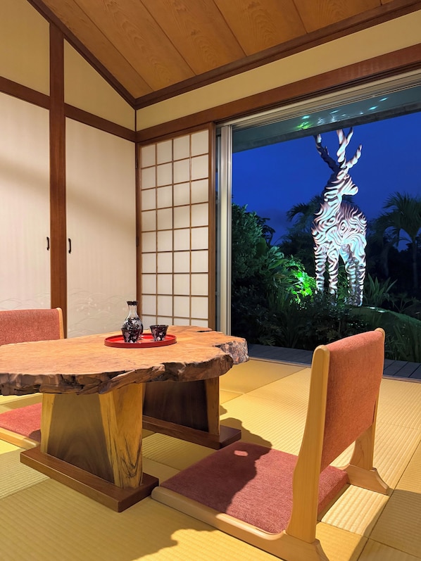 A traditional Japanese room with tatami flooring, a wooden table, and a sliding door leading to a garden.