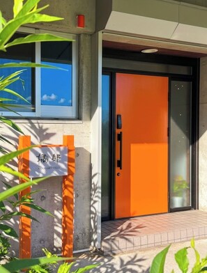 Ein moderner Gebäudeeingang mit einer leuchtend orangefarbenen Tür, einem Schild und einem Betonbau.