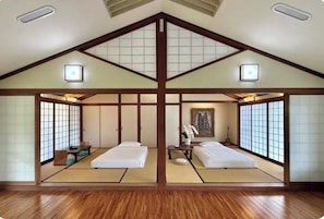 Et traditionelt japansk værelse med tatamimåtter, to senge, skydedøre og et maleri på væggen.