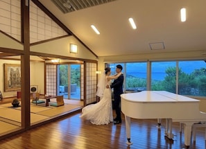 A wedding ceremony in a room with a piano, tatami mats, and a view of the sea.