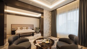 A hotel room with a bed, two armchairs, a coffee table, and a large window with curtains. - Ananta Express (Katra)