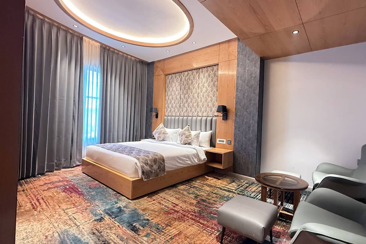 A modern hotel room with a large bed, a seating area, and a patterned carpet.