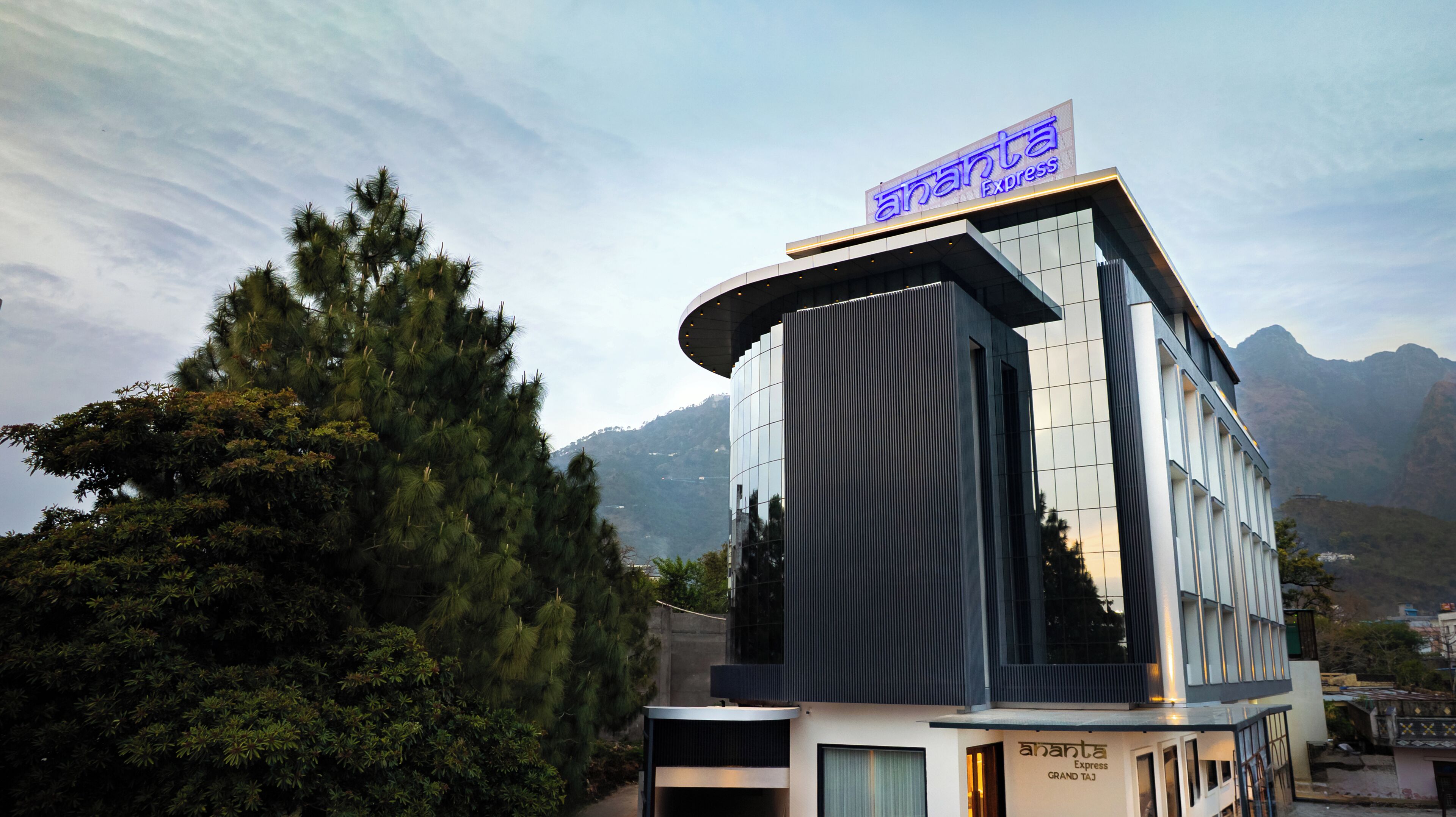 A modern hotel with a prominent sign reading 'Ananta Express.' It features a curved facade with large windows and a flat roof.