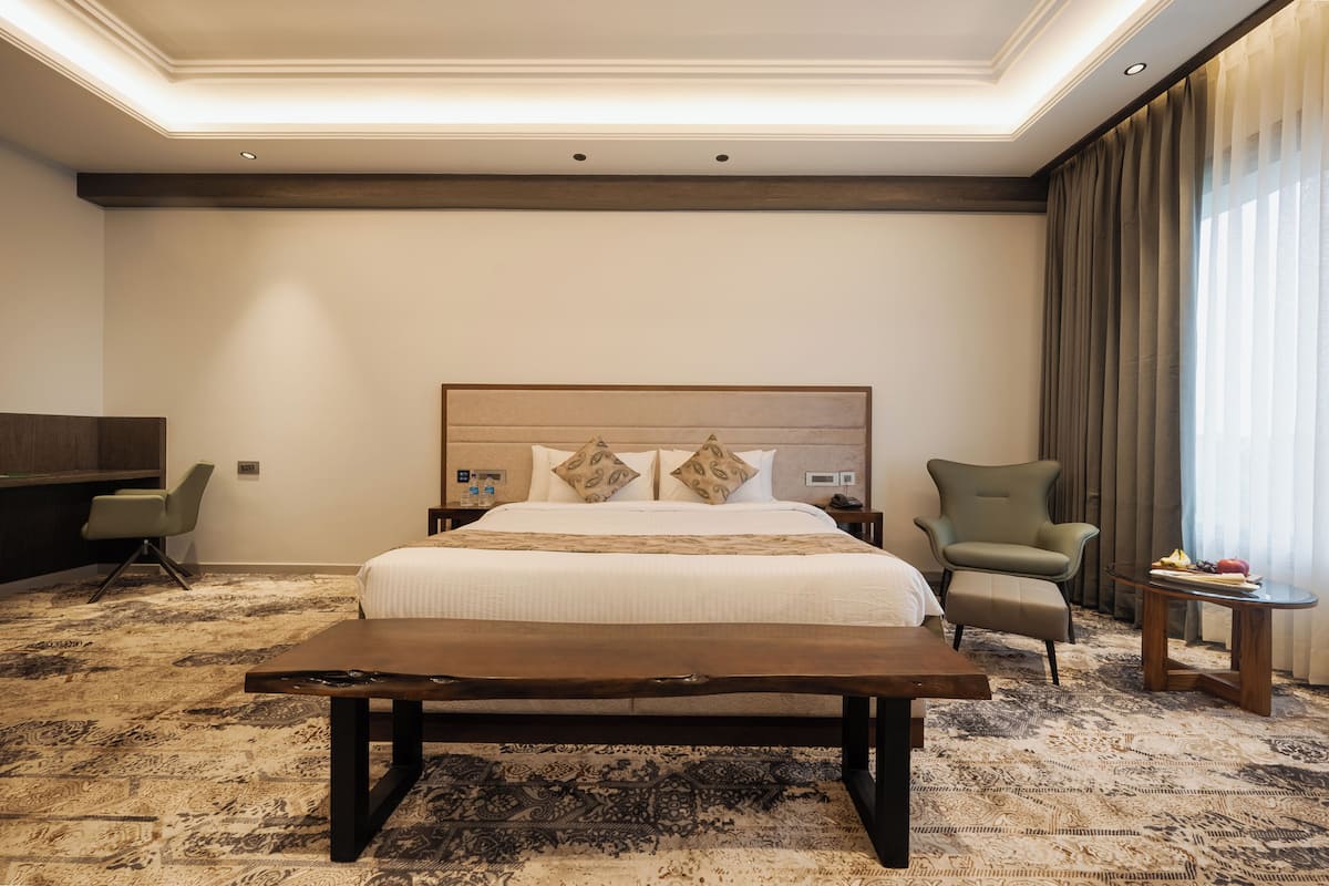 A hotel room with a large bed, a wooden bench, a desk, and a chair.