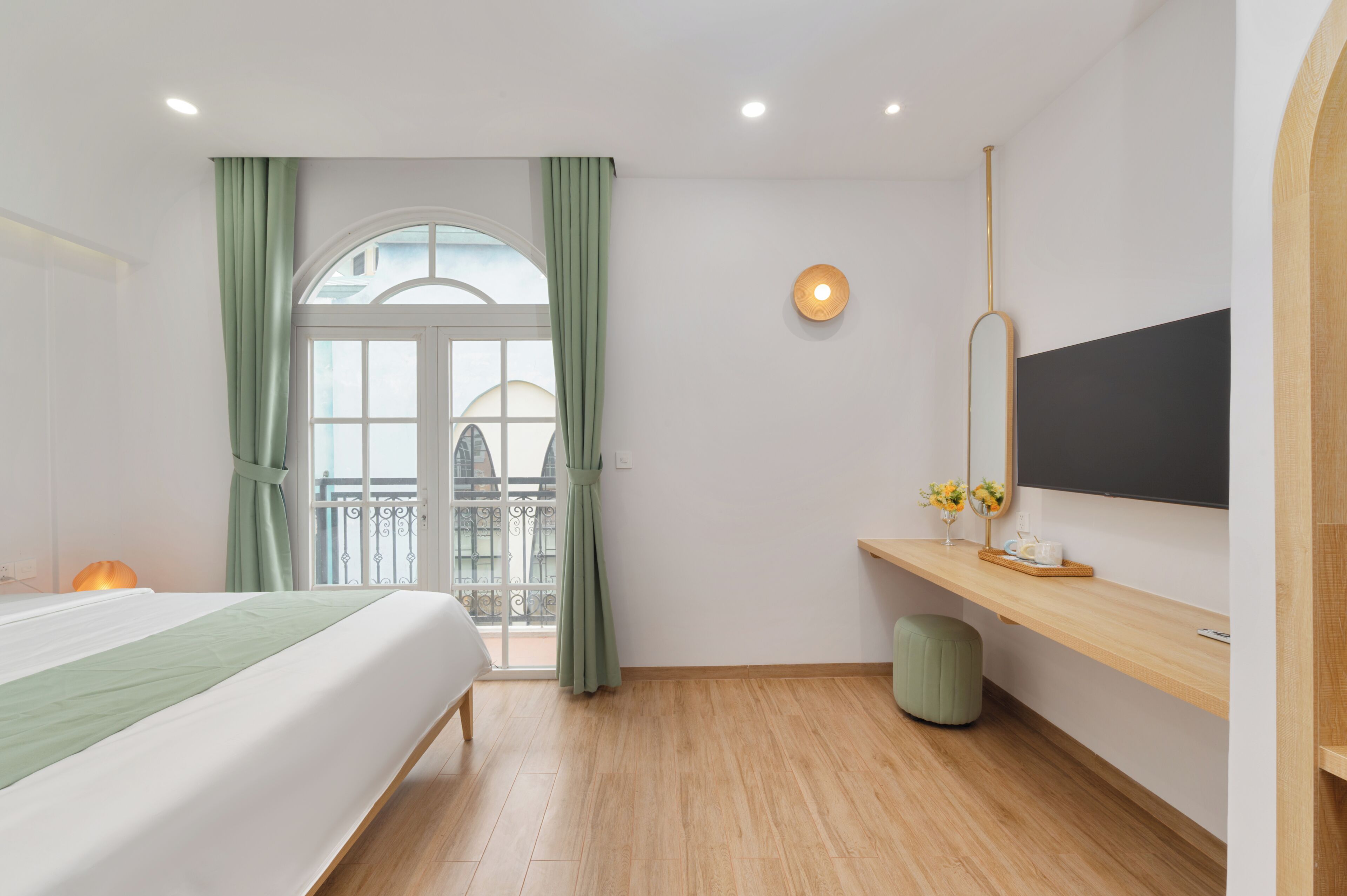 Habitación de hotel con cama, escritorio con televisor de pantalla plana, taburete pequeño y ventana con cortinas.