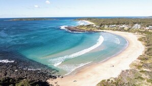 Paesaggio costiero con acque trasparenti, una spiaggia sabbiosa e una zona residenziale con case.