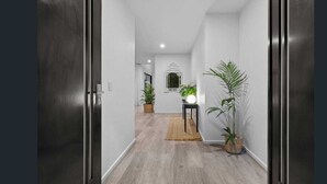 A hallway with a wooden floor, a small table with a lamp, and potted plants. - Longboard Coastal Retreat (Kingscliff)